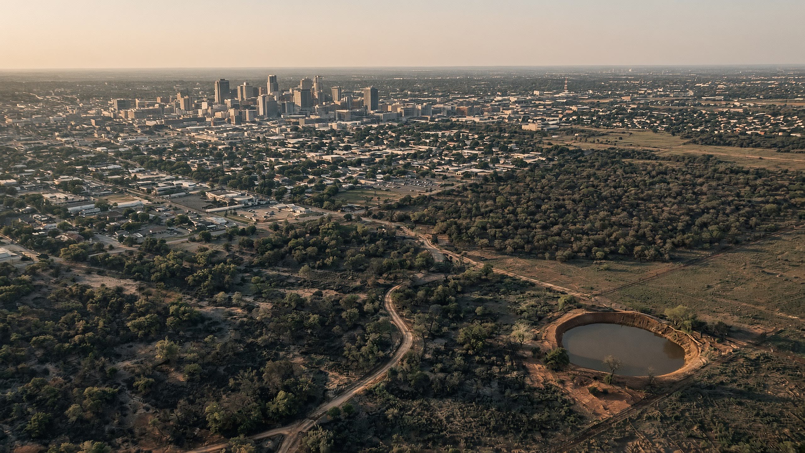 From the air. A big city of roofs and towers meeting brush, pasture, and a stock tank.